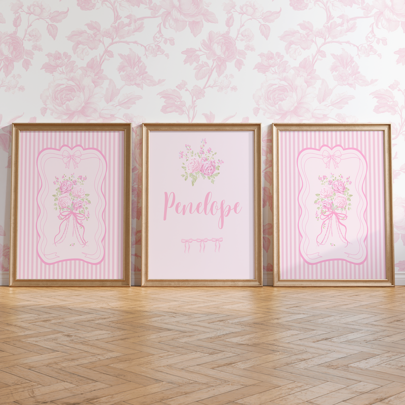 Three framed pink prints with floral designs and names on a wall with matching pink floral wallpaper.
