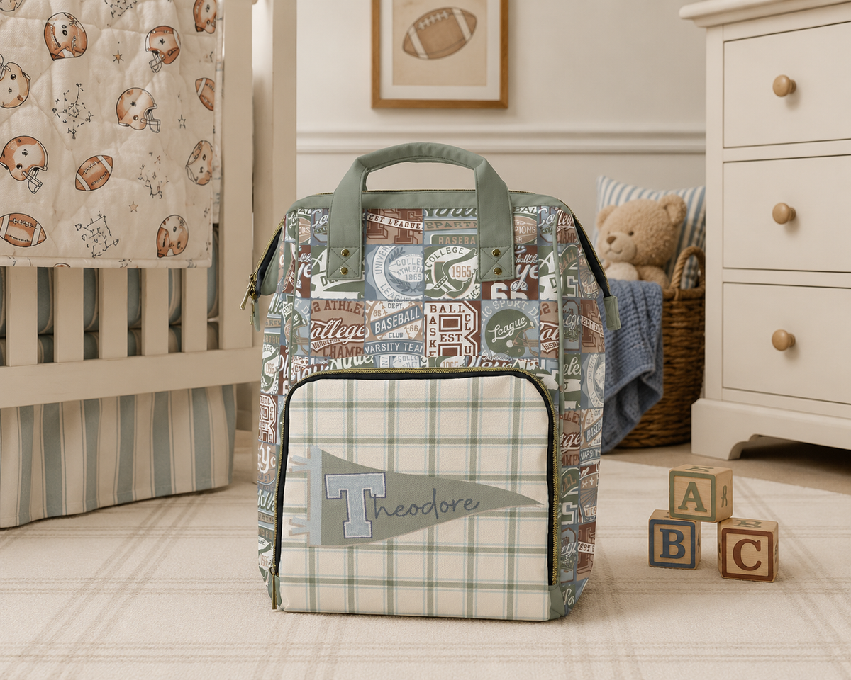 A personalized sports-themed diaper bag with a collegiate patchwork pattern and a green plaid front pocket, displayed in a styled nursery setting.