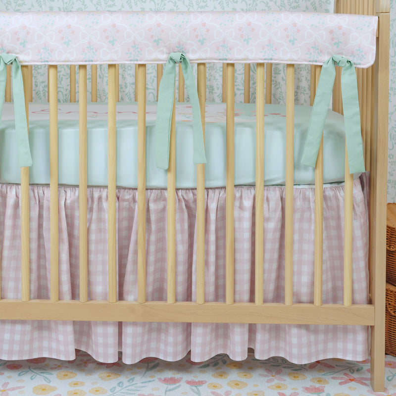 Wooden crib with white mattress and green bumper, light blue wall with floral wallpaper, wicker basket.