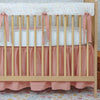 Wooden crib with pink bedding and white mattress in a room with floral wallpaper.