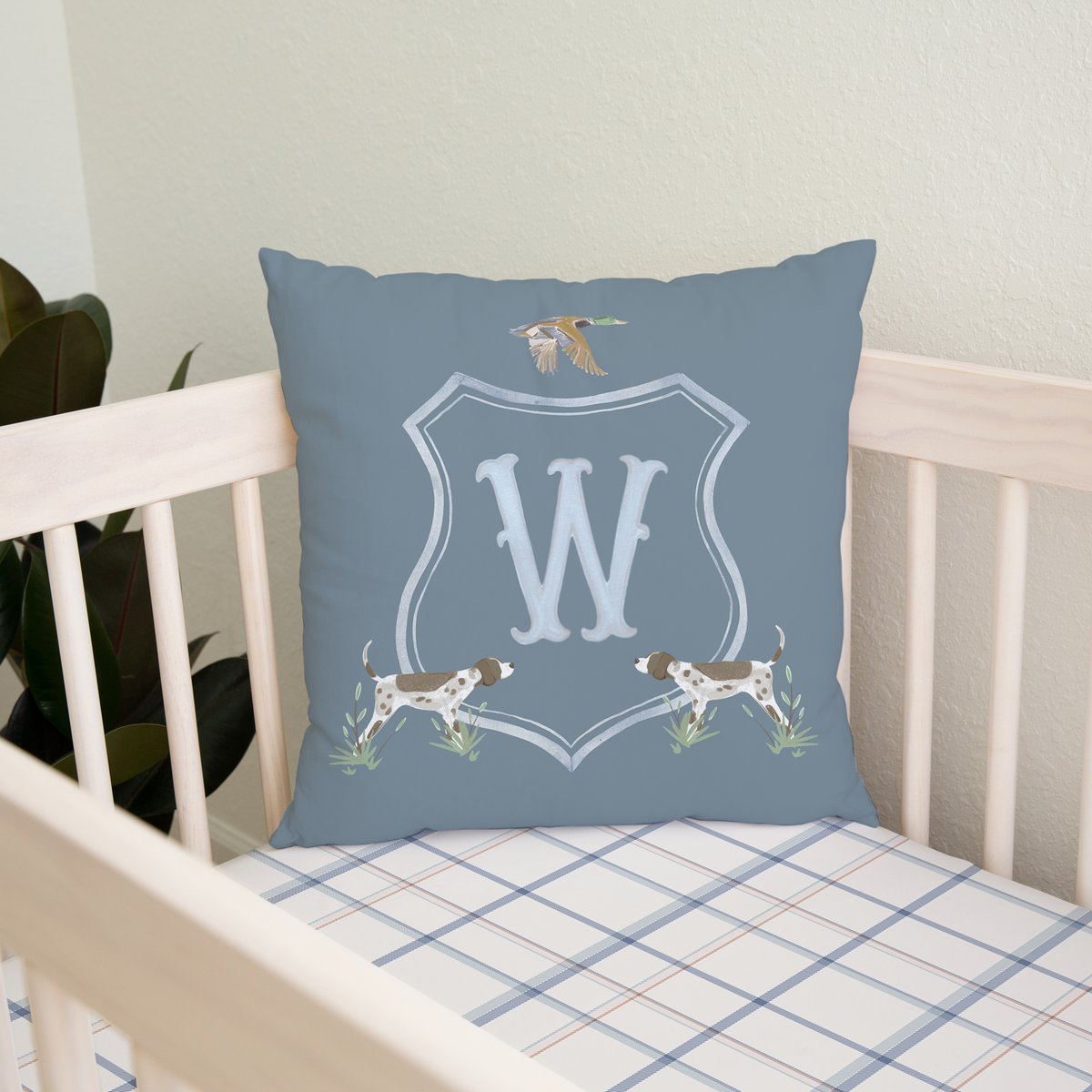 Blue pillow with a monogram 'W' on a crib with checkered bedding.