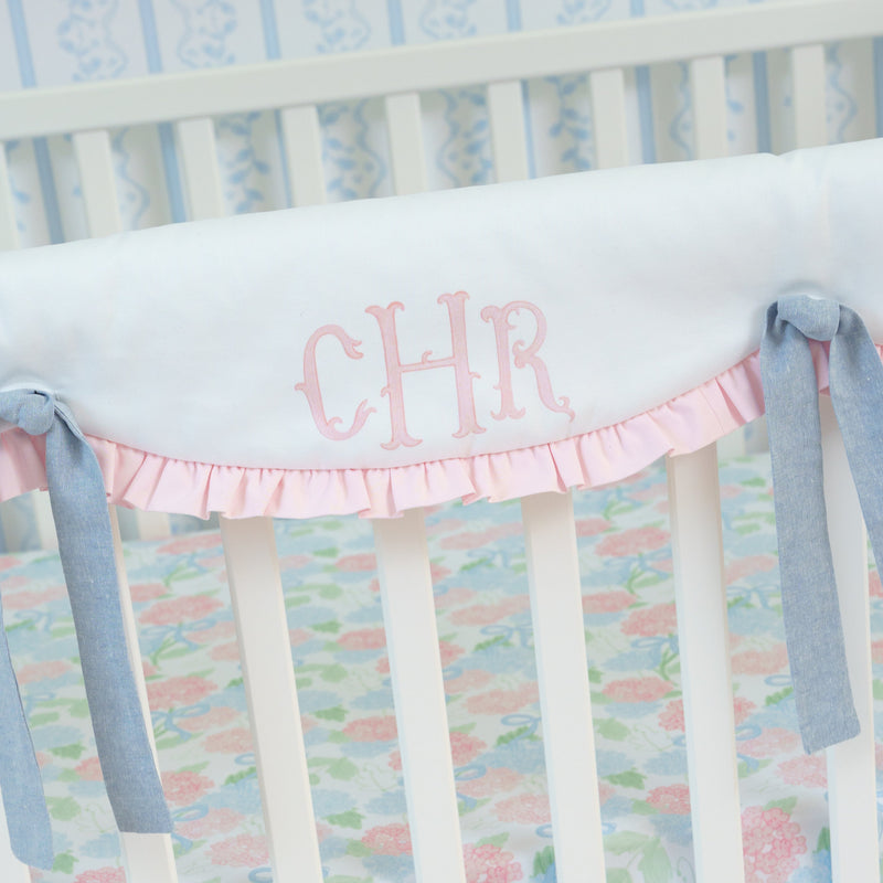 Baby crib with floral bedding and pink ruffles, featuring the name 'CHR' on a white background.