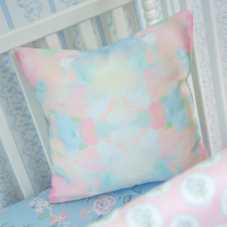Pastel watercolor pillow and pink floral crib sheet on a crib with white railings.