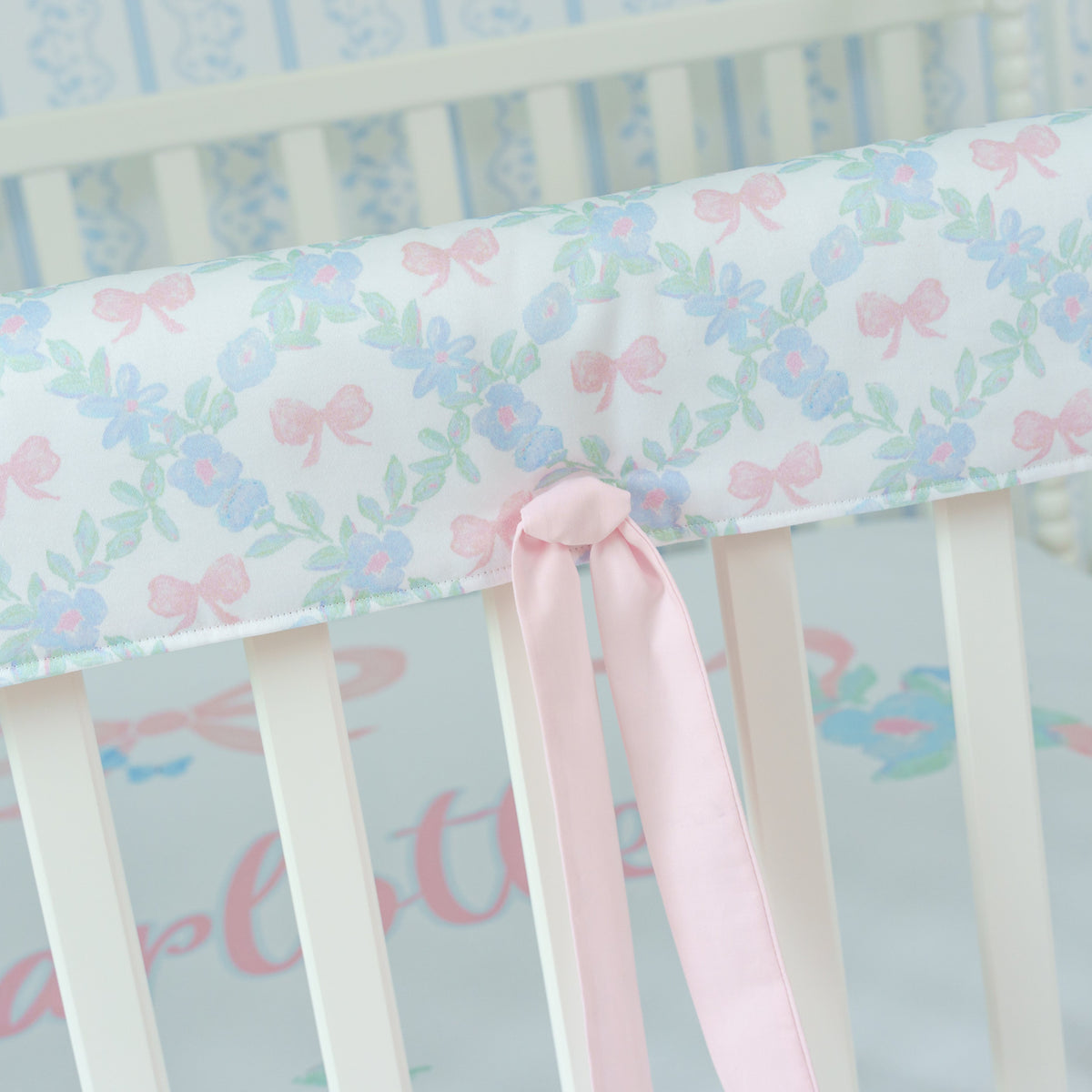 Crib rail cover with floral pattern and pink bow on a white crib