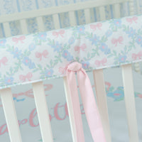 Crib rail cover with floral pattern and pink bow on a white crib
