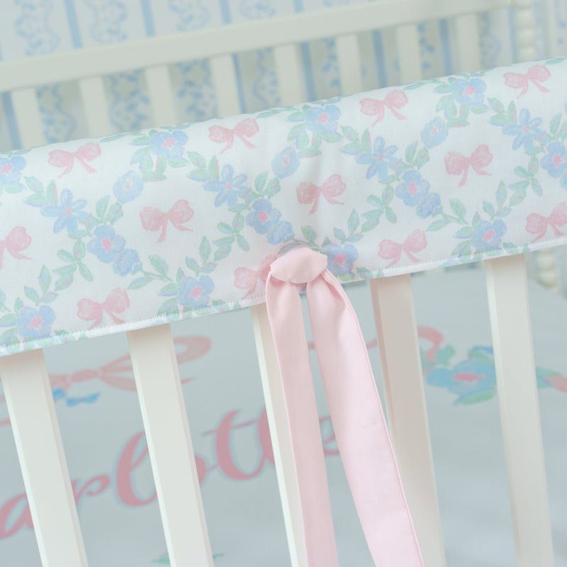 Crib rail cover with floral pattern and pink bow on a white crib