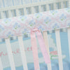 Crib with floral-patterned bumper and pink ribbon, on a light blue background