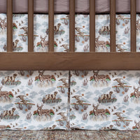 Crib with wooden sides and a white sheet featuring deer and nature patterns.