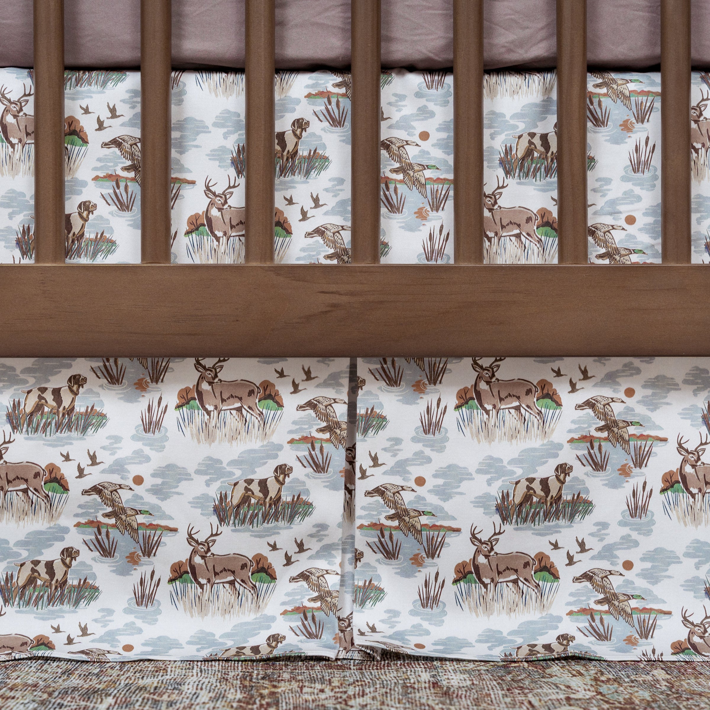 Crib with wooden sides and a white sheet featuring deer and nature patterns.