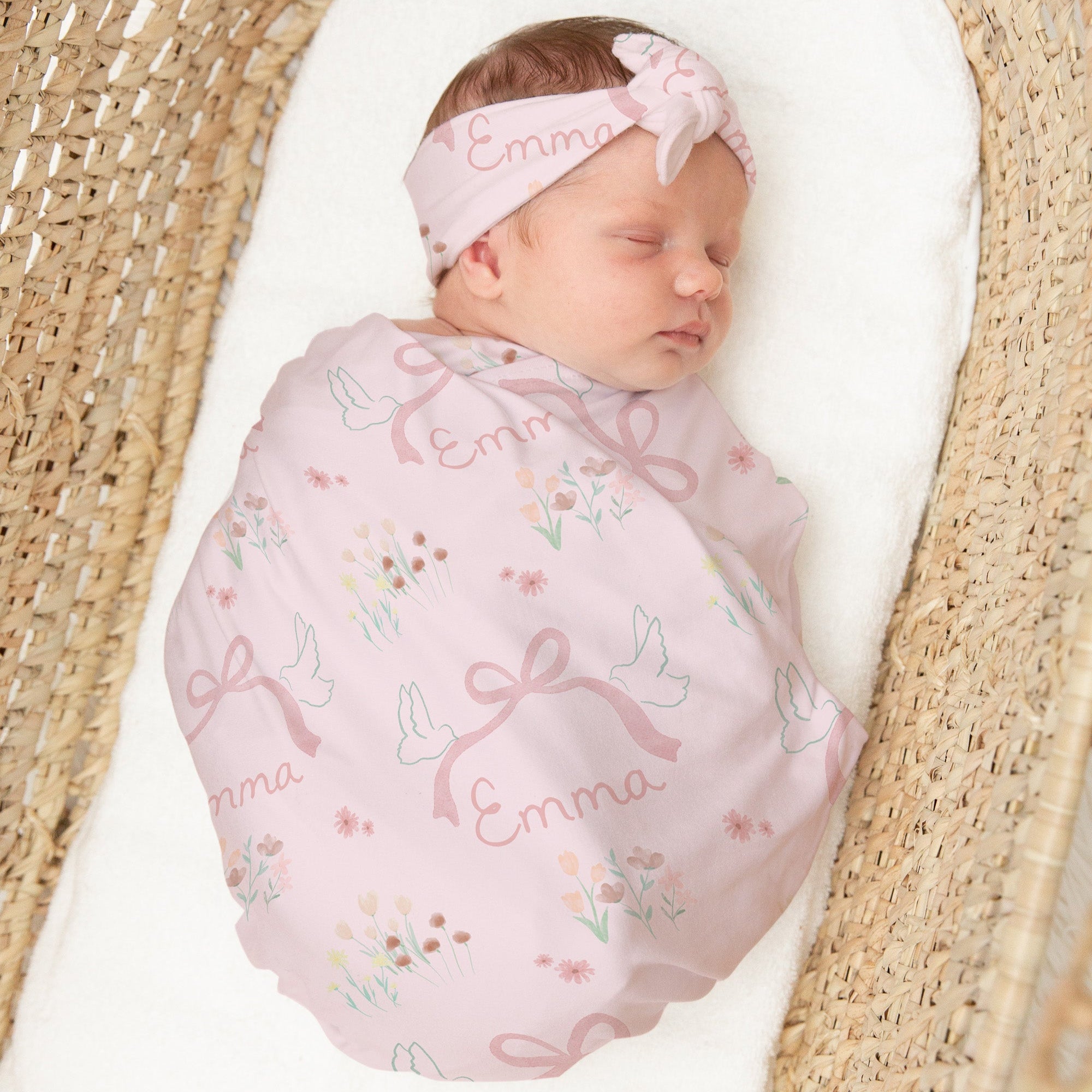 Newborn baby wrapped in a pink blanket with floral patterns and a matching headband, lying in a woven basket.