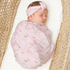Newborn baby wrapped in a pink blanket with floral patterns and a matching headband, lying in a woven basket.