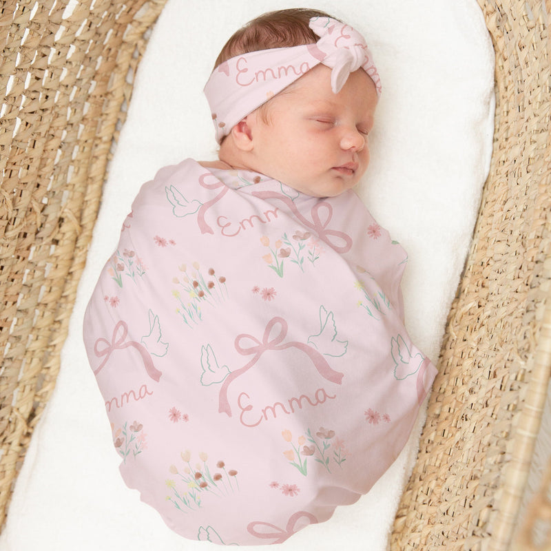 Newborn baby wrapped in a pink blanket with floral patterns and a matching headband, lying in a woven basket.