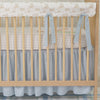 Nursery crib with beige wooden frame, white mattress, and gray bedding in a room with framed artwork on the wall.