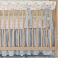 Nursery crib with beige wooden frame, white mattress, and gray bedding in a room with framed artwork on the wall.
